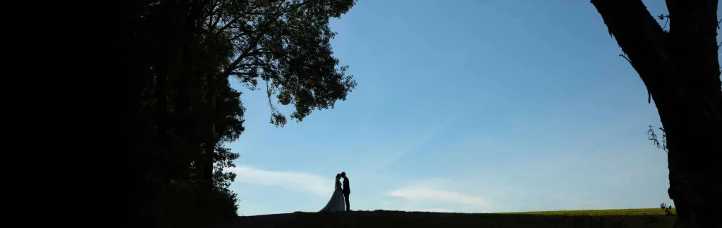 Silhouette vom Brautpaar umarmt am Feldrand vor blauem Himmel